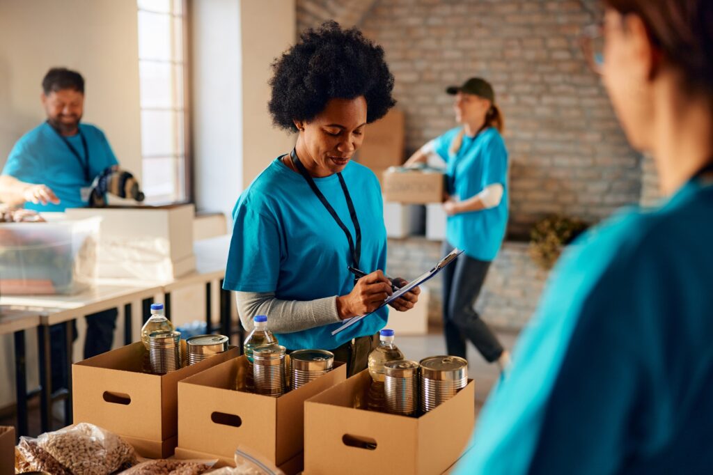 Black female volunteer making list of food supplies while working at humanitarian aid center.